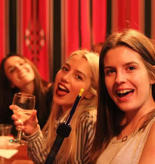 Three friends laughing at a lounge table, glasses raised, a shisha pipe between them