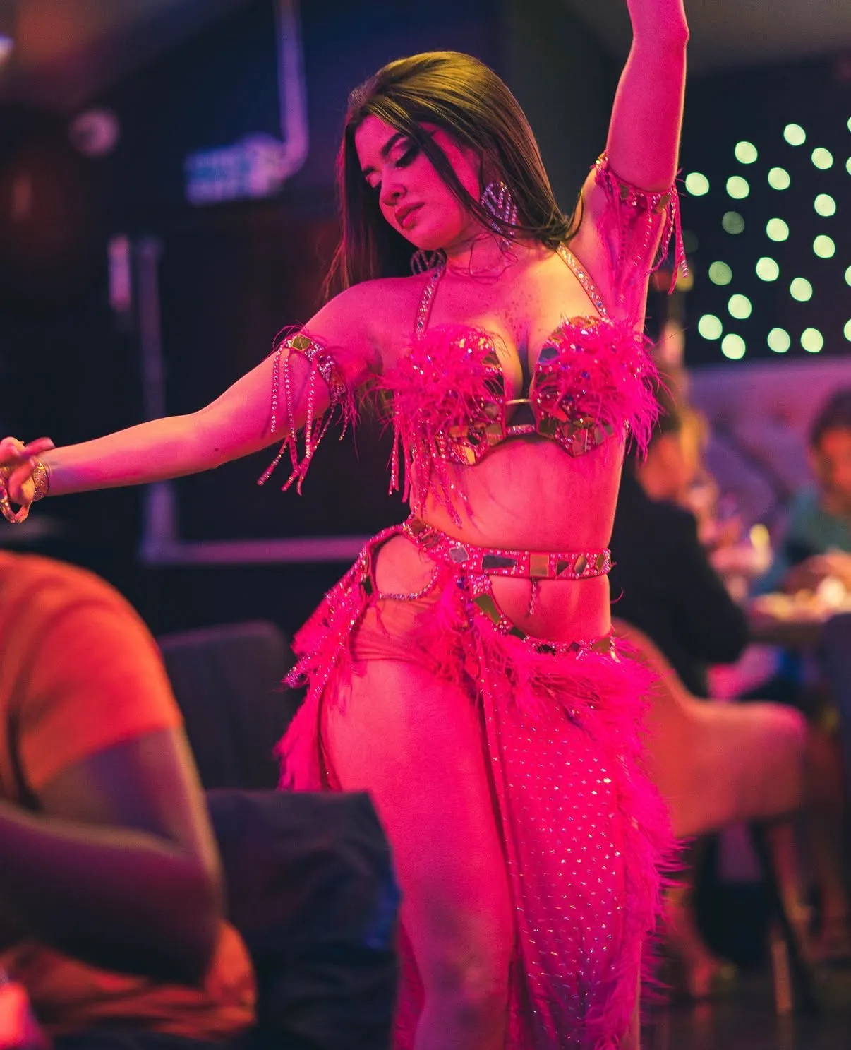 A belly dancer in a pink feathered costume performing between the tables at Nana's